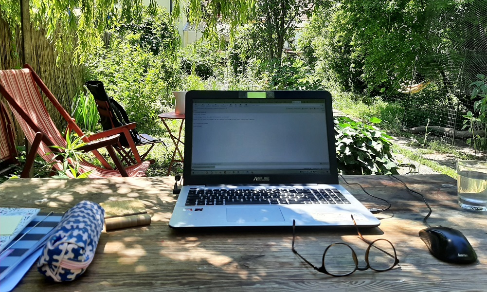 Ein Laptop auf einem Schreibtisch mitten im Grünen unter Bäumen