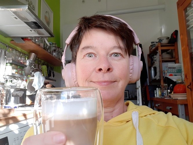 Frau in gelbem Pulli mit Kopfhörer und Tasse Kaffee