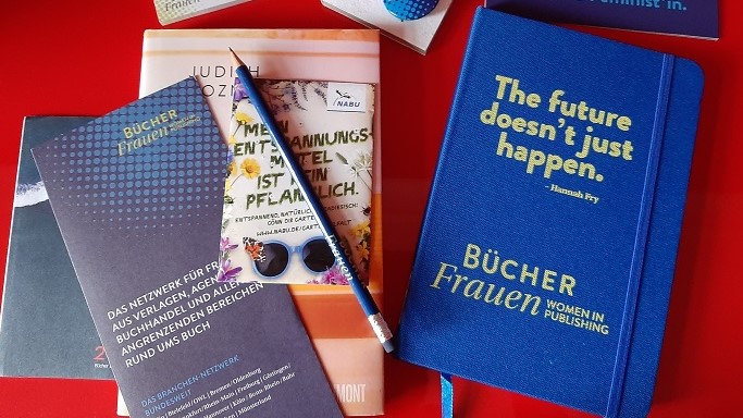 ein blaues Buch, ein Flyer und ein Bleistift liegen auf einem Tisch