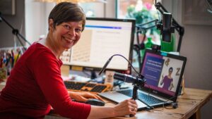Frau sitzt am Schreibtisch vor Laptop und Mikrofon
