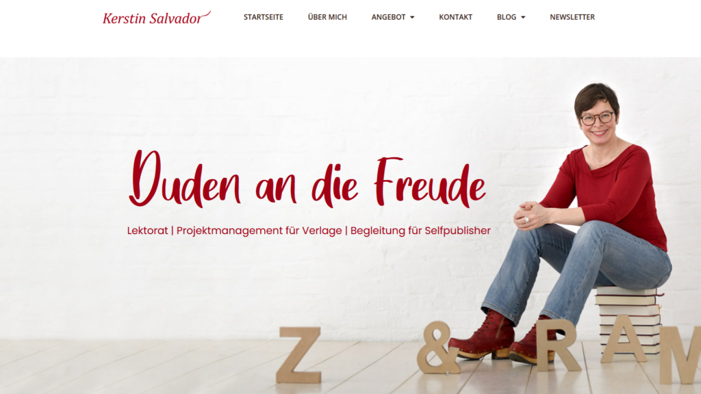 Kerstin Salvador sitzt auf einem Bücherstapel vor einem hellen Hintergrund. Neben ihr liegen und stehen große Pappbuchstaben. Im Bild steht der Claim „Duden an die Freude“.